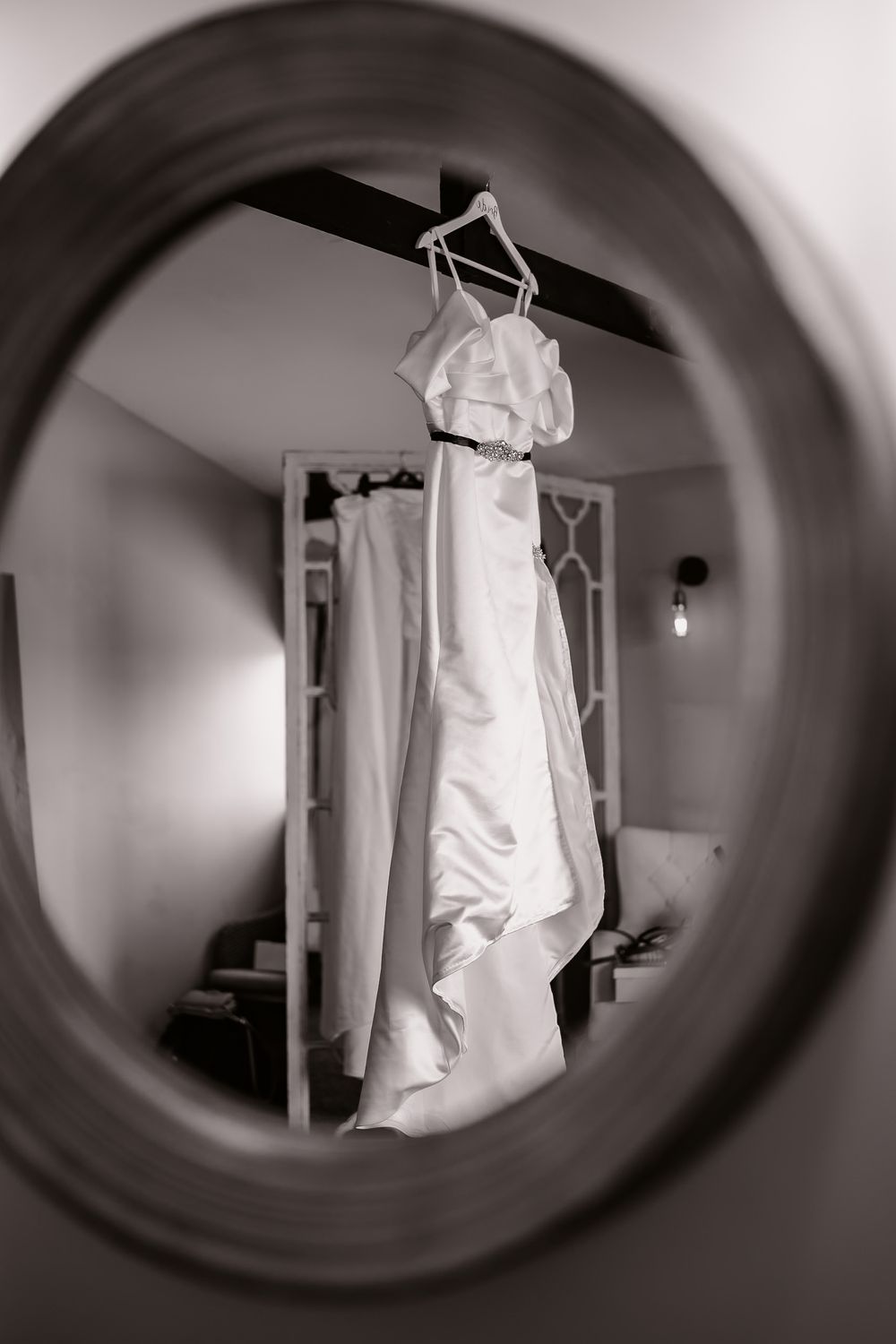 White wedding dress hanging in mirror reflection creating artistic composition.