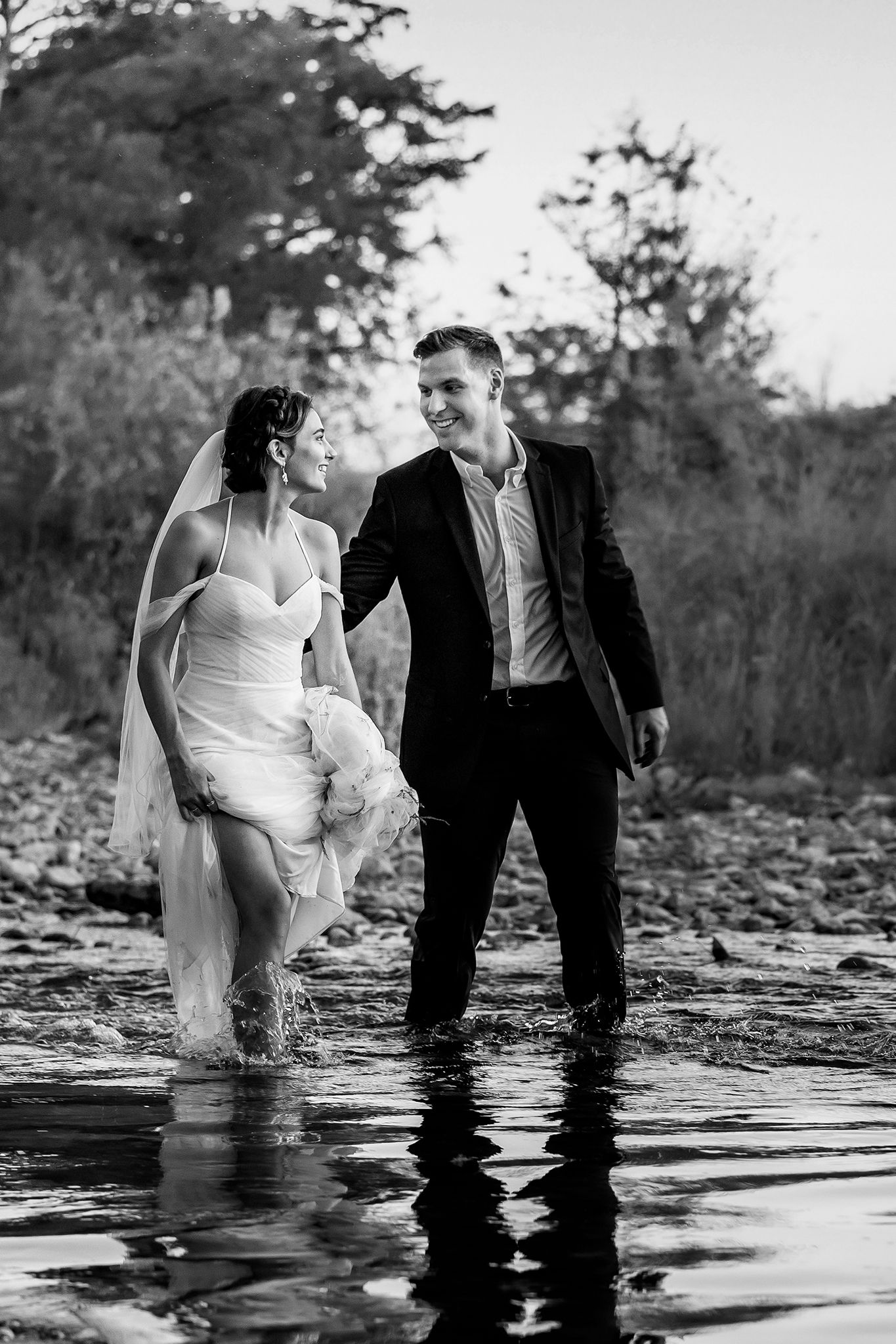 A couple stands together in shallow water during their black and white wedding photo session.