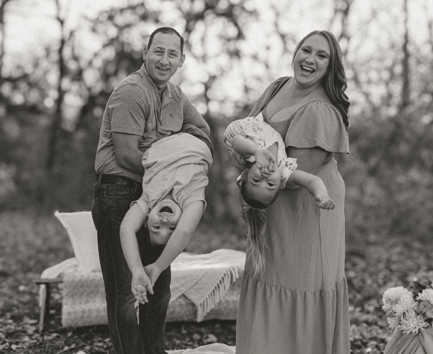A couple in casual attire poses together outdoors during a black and white photo session in a natural setting.