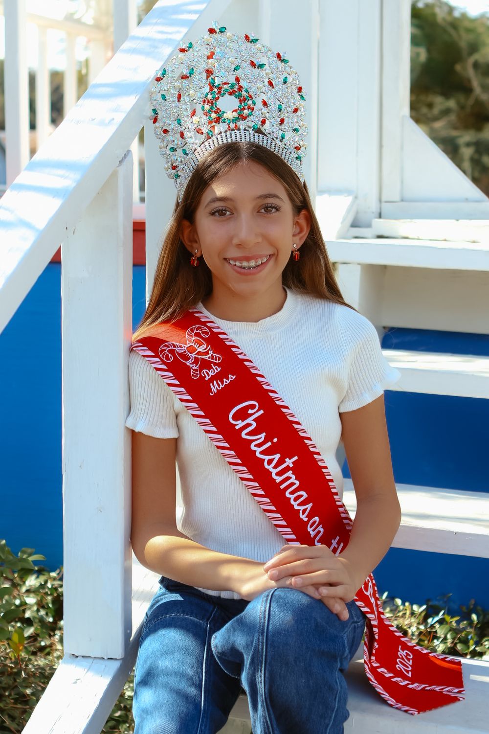 Person wearing white shirt and jeans sits on white porch railing with red sash.