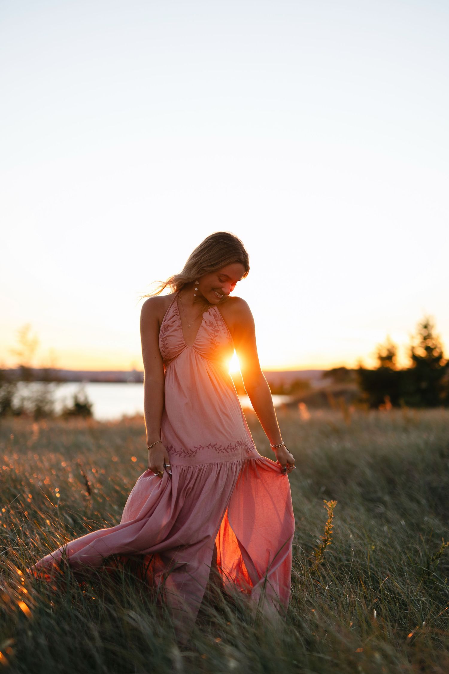 A person in a flowing pink dress sits in a golden field at sunset as sunlight creates a warm ethereal glow.