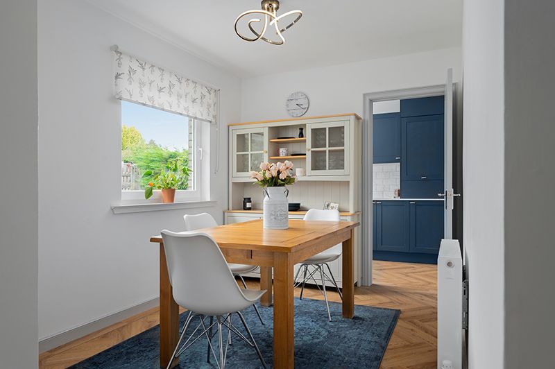 Modern kitchen and dining area with white cabinets, wood floors, and navy blue accent wall showcasing multiple room angles.