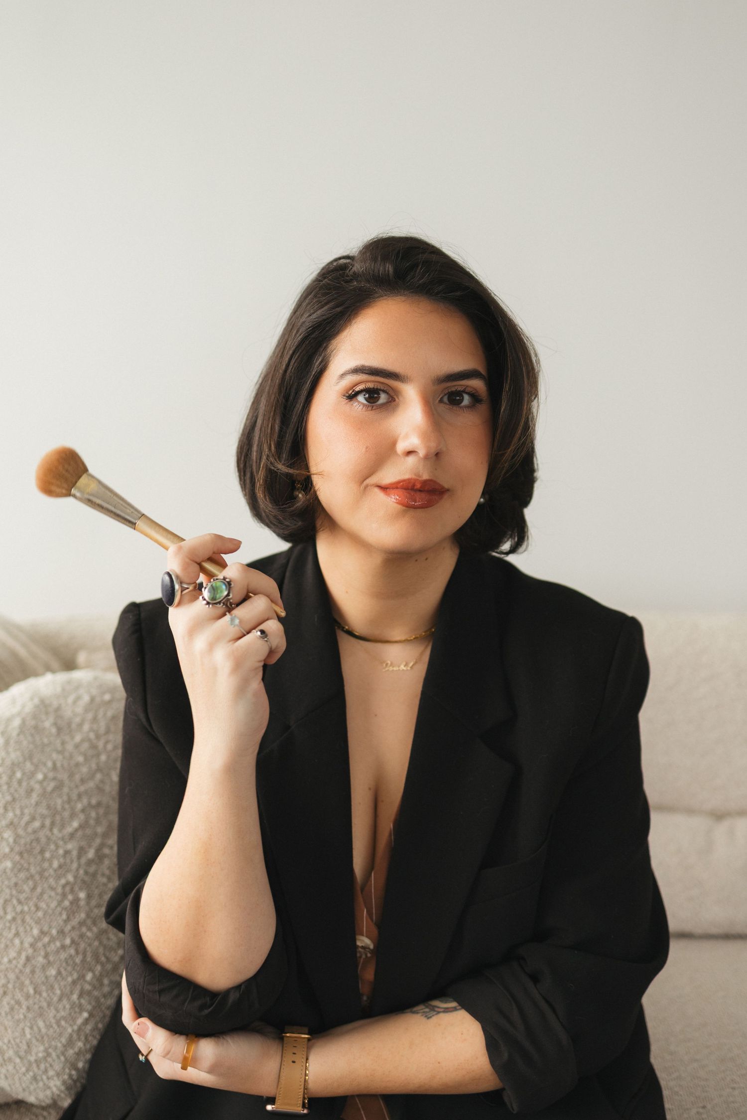 A professional portrait session featuring black blazer and makeup brush against white background.