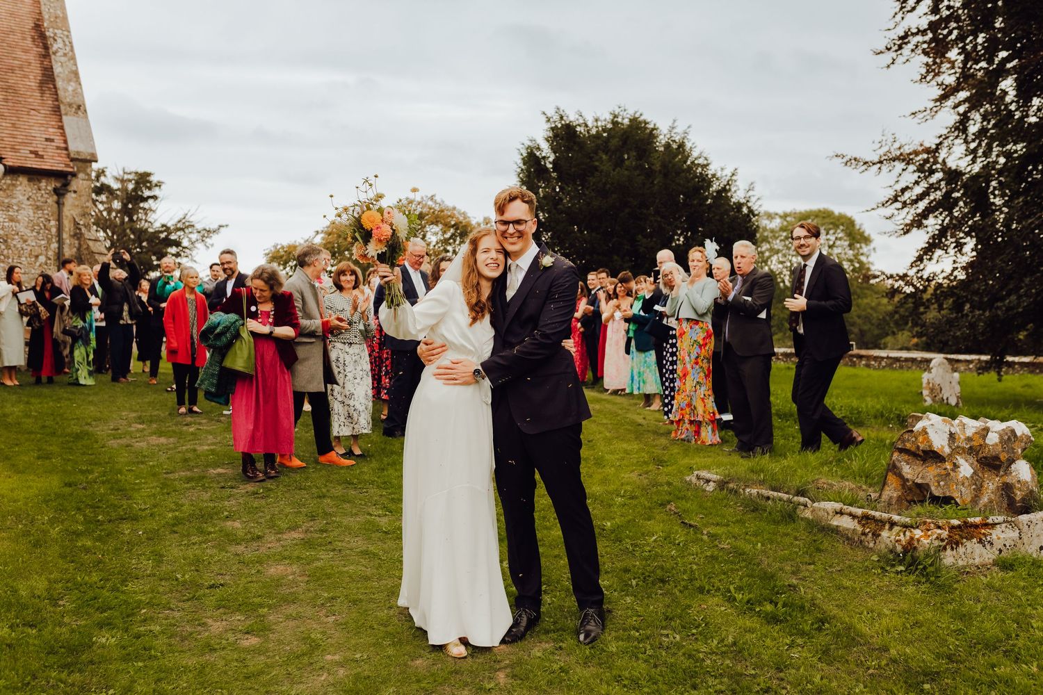A wedding couple outside a church with their guests in the background, documentary wedding photography in Hampshire