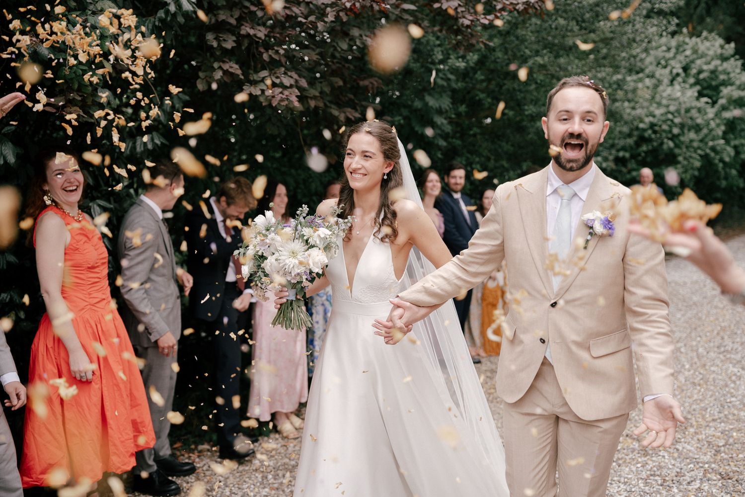Wedding party celebrates outdoors in soft peach and neutral colored attire during summer garden celebration.