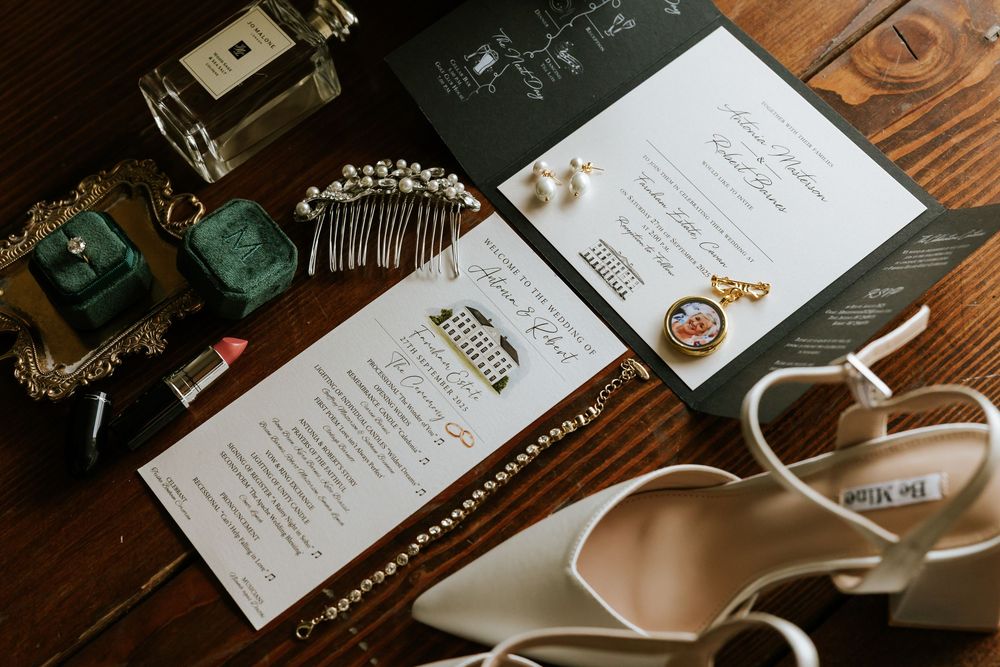 Wedding details including invitation cards, perfume bottles, hair accessories and bridal shoes arranged on wooden surface. Farnham estate