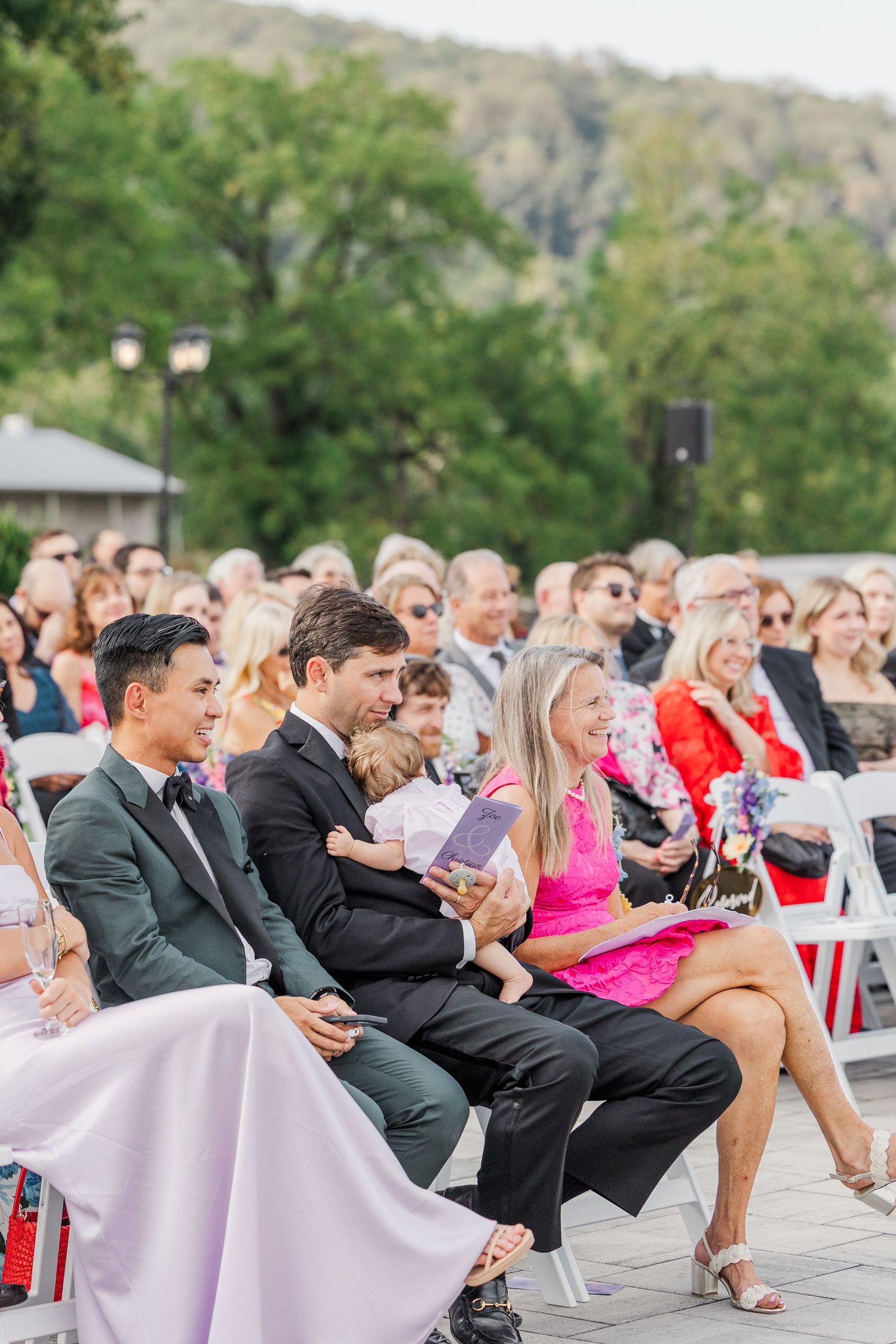 Large group of wedding guests seated in white chairs at outdoor venue.