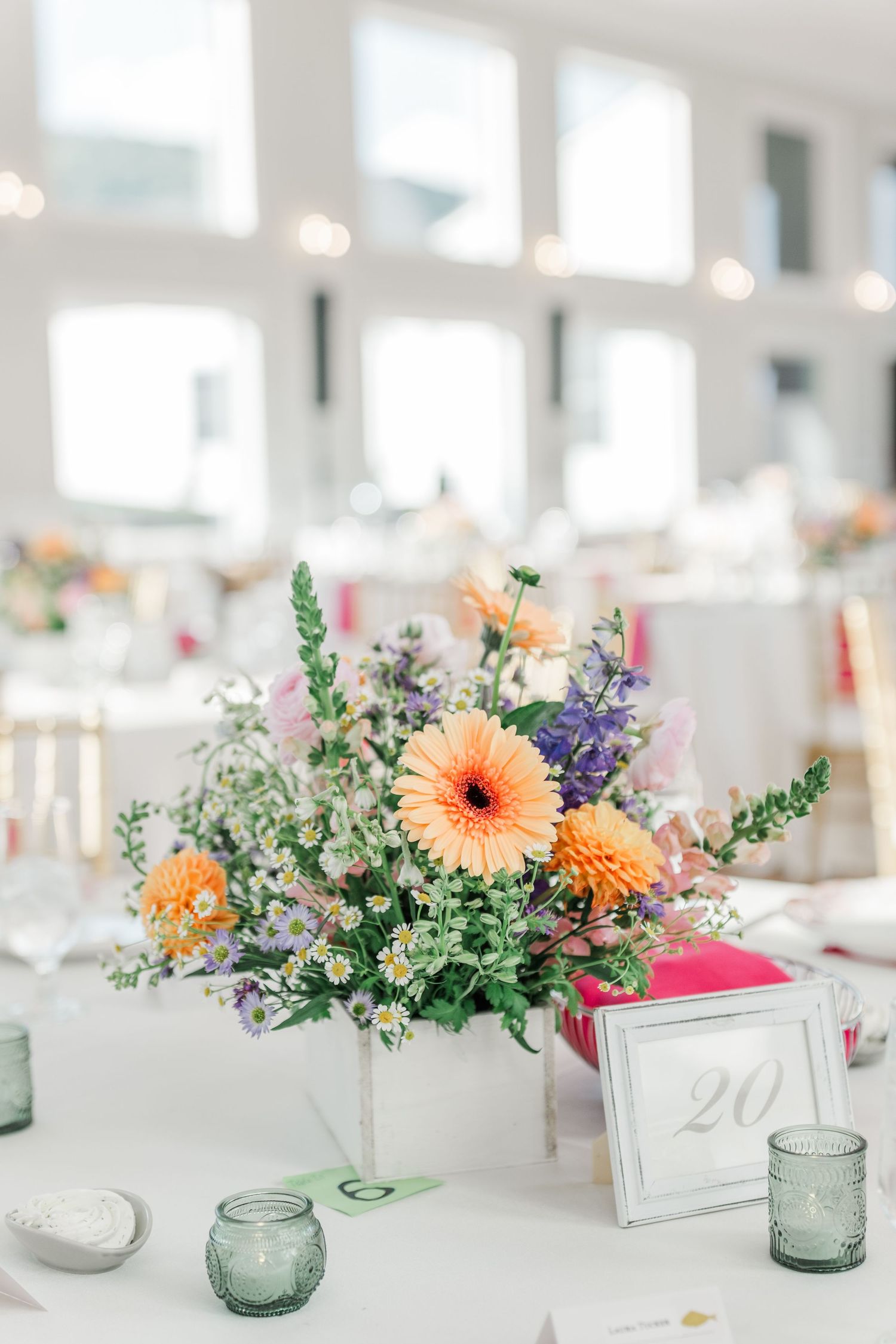 Wedding reception centerpieces featuring colorful flowers, greenery and blue glass votives on white tablecloths.