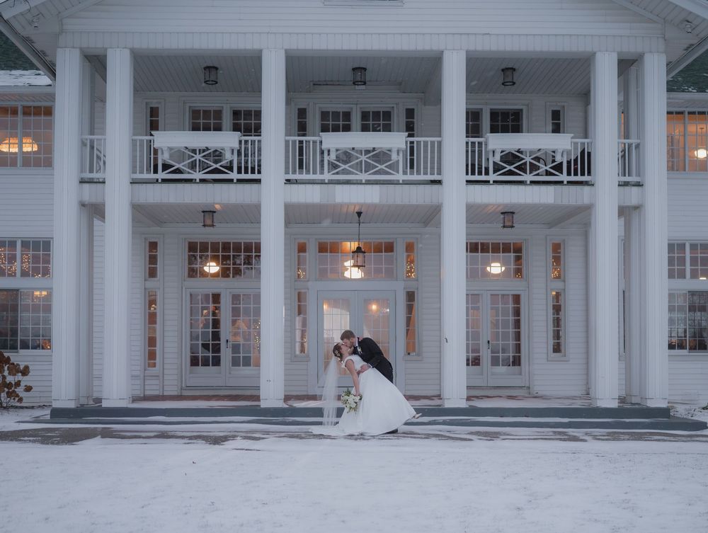 A grand white colonial-style building with tall columns and a wrap-around porch lit up at dusk.