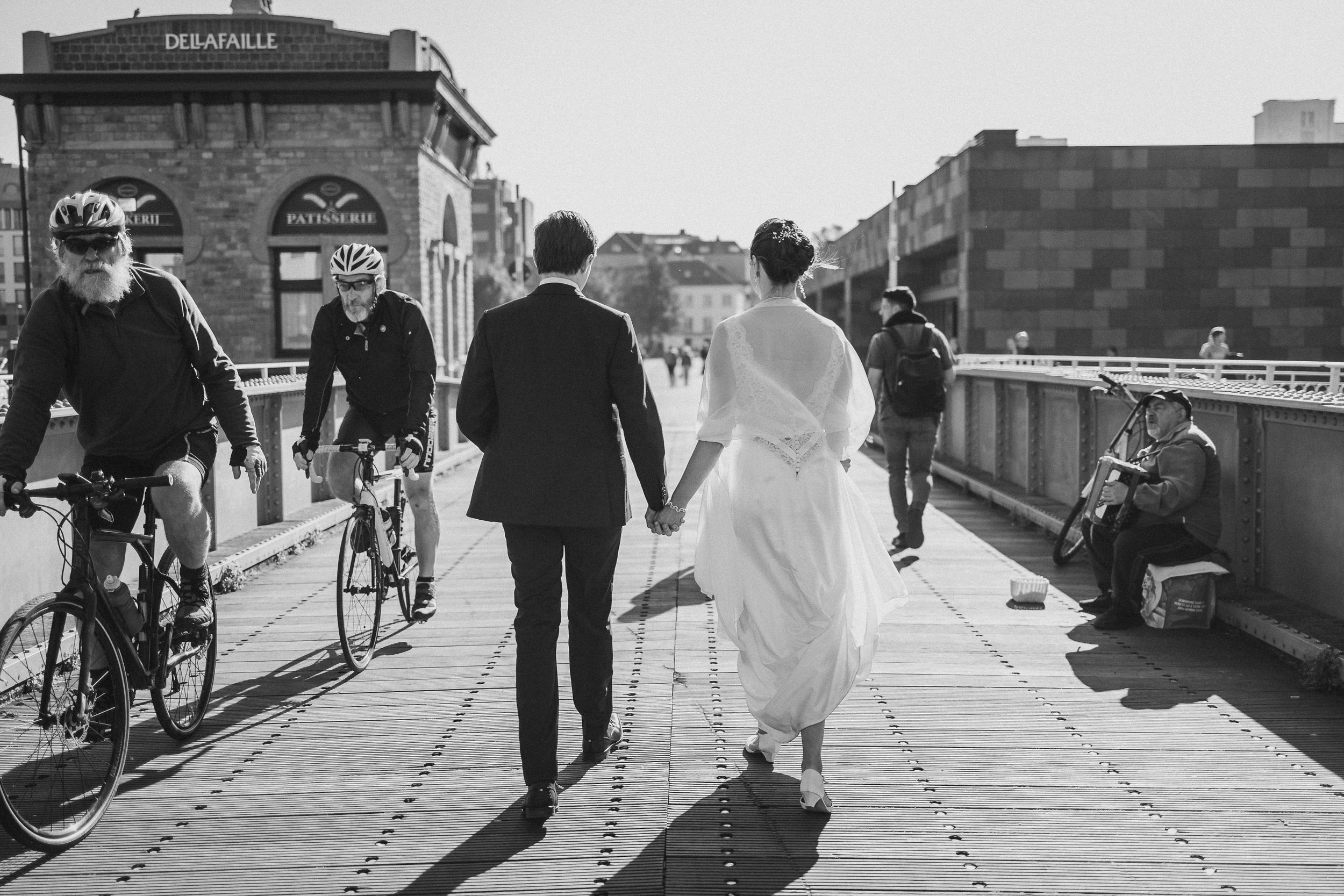 Wedding couple walking along a scenic pathway with brick buildings in the background.
