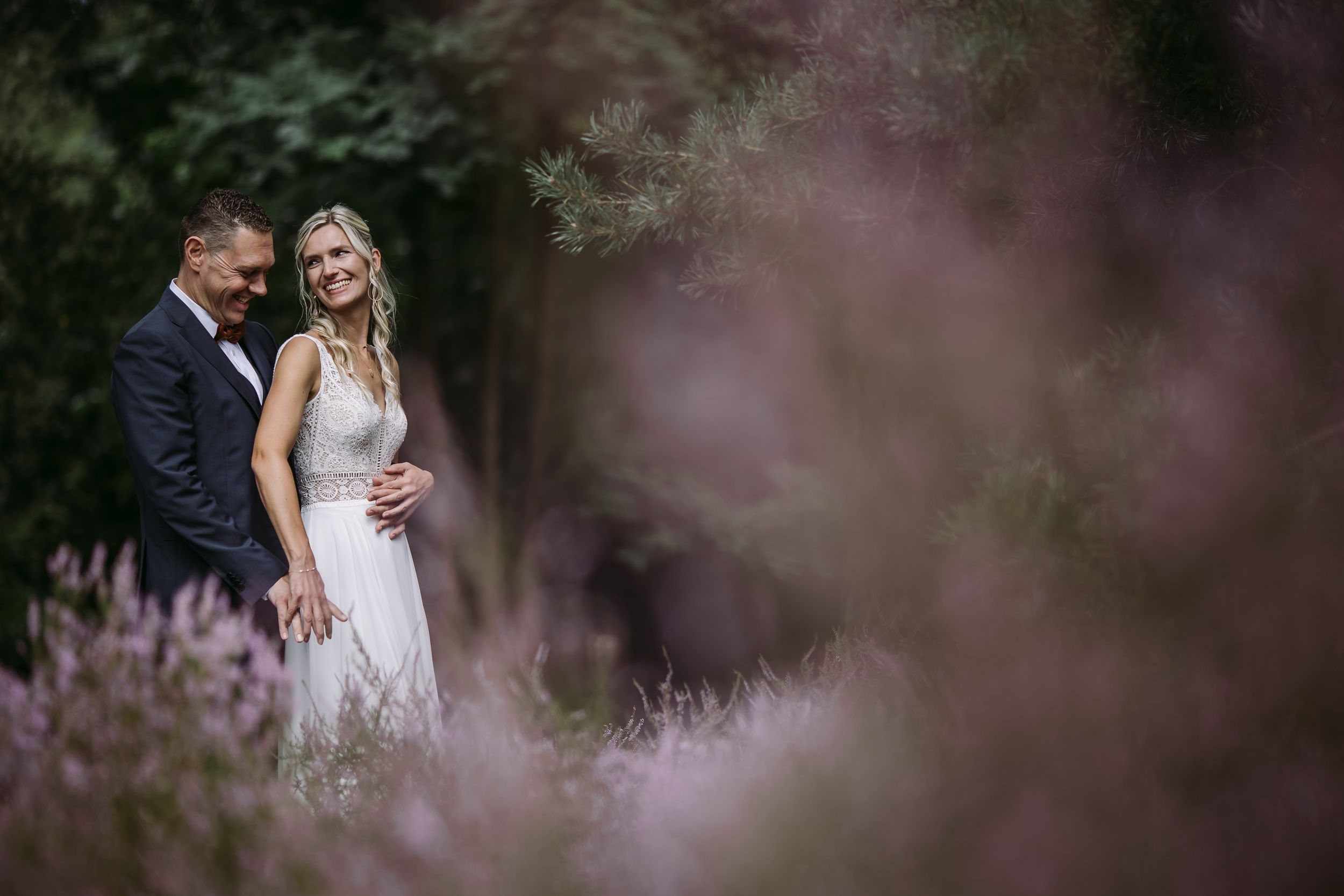 Wedding portraits set against blurred purple wildflowers in a dreamy outdoor setting.