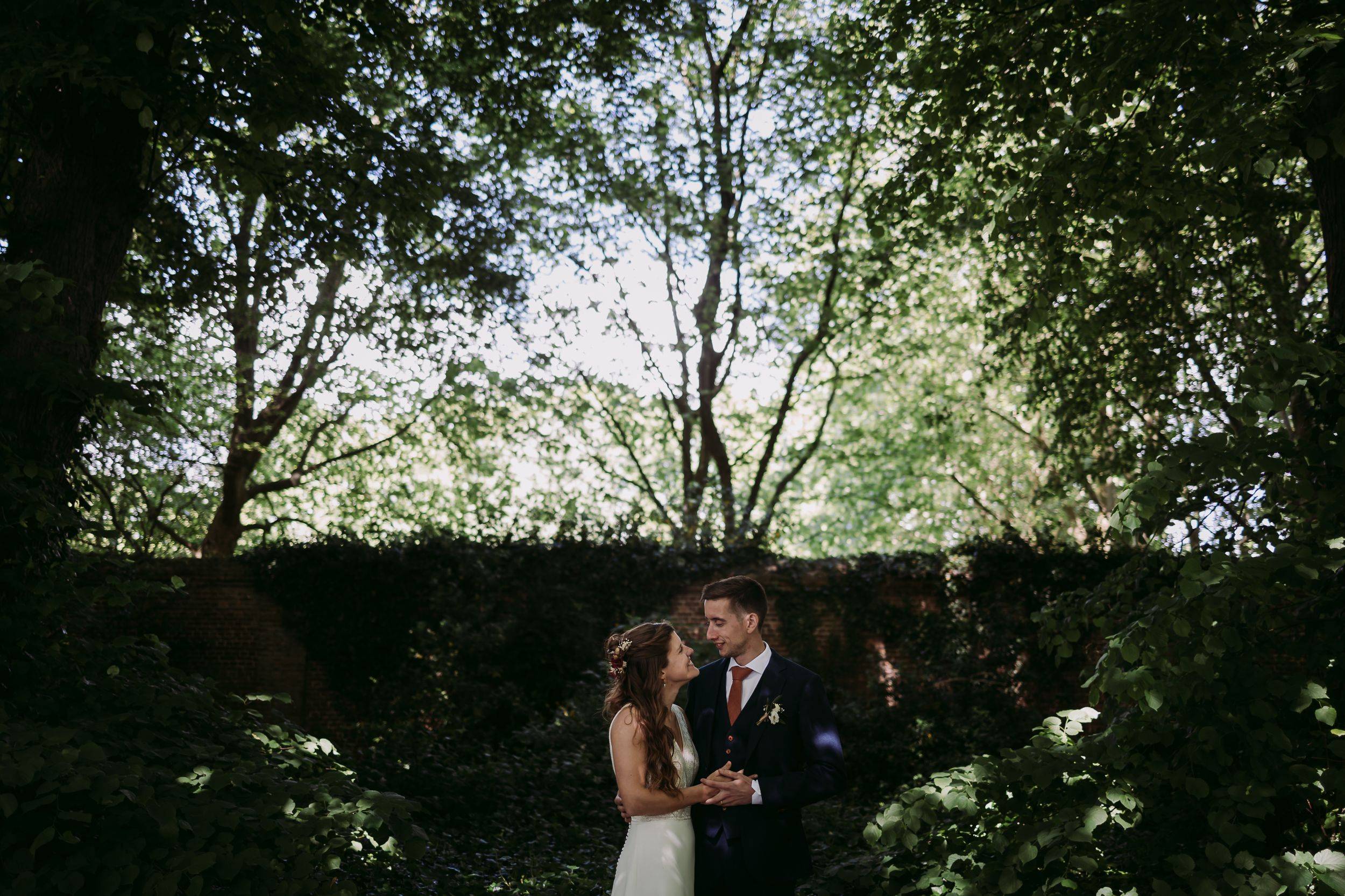 Romantic wedding portraits captured through tree branches with soft natural lighting.