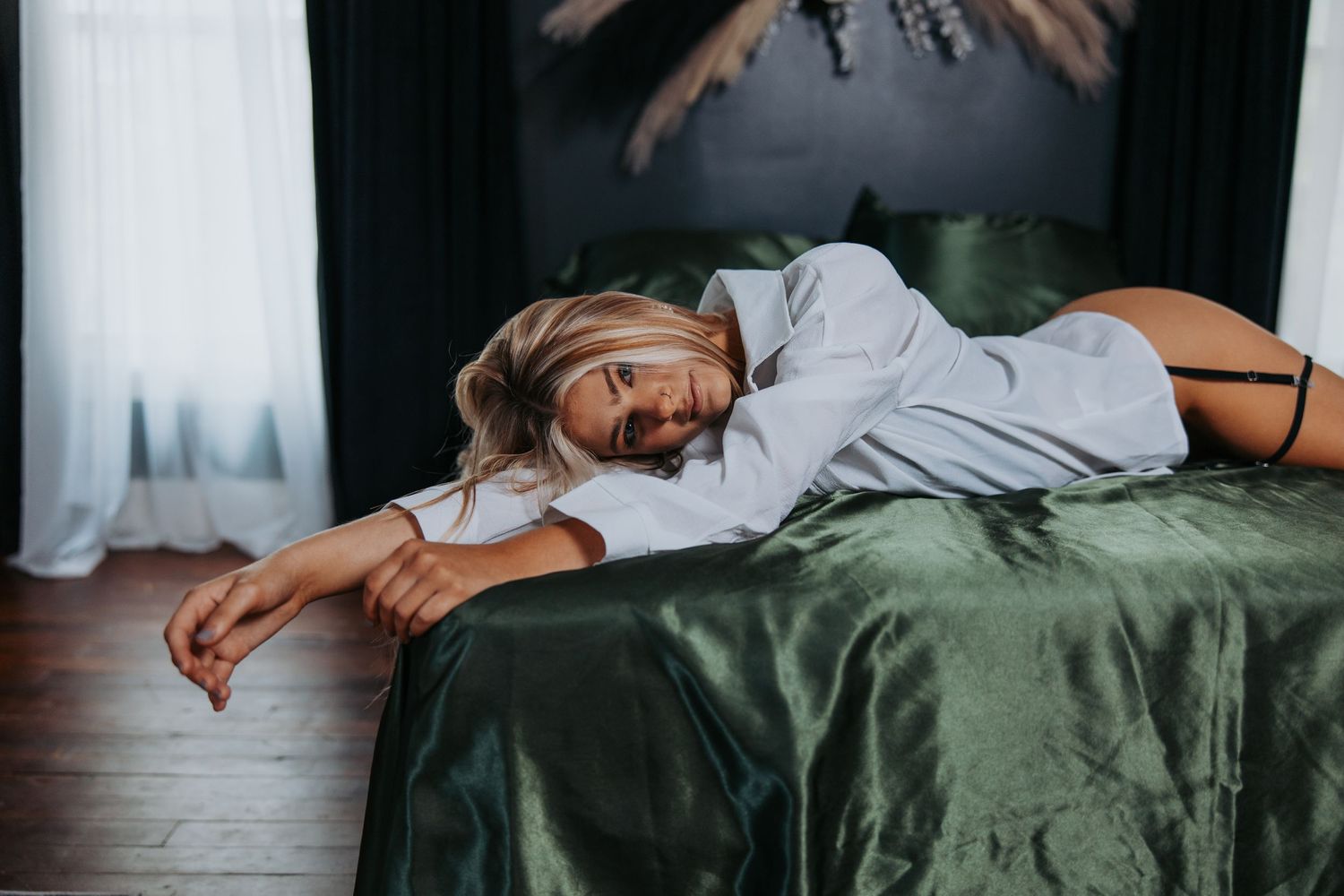 Someone in a gray sweater lying relaxed on a bed with emerald green silk bedding in a cozy bedroom setting.