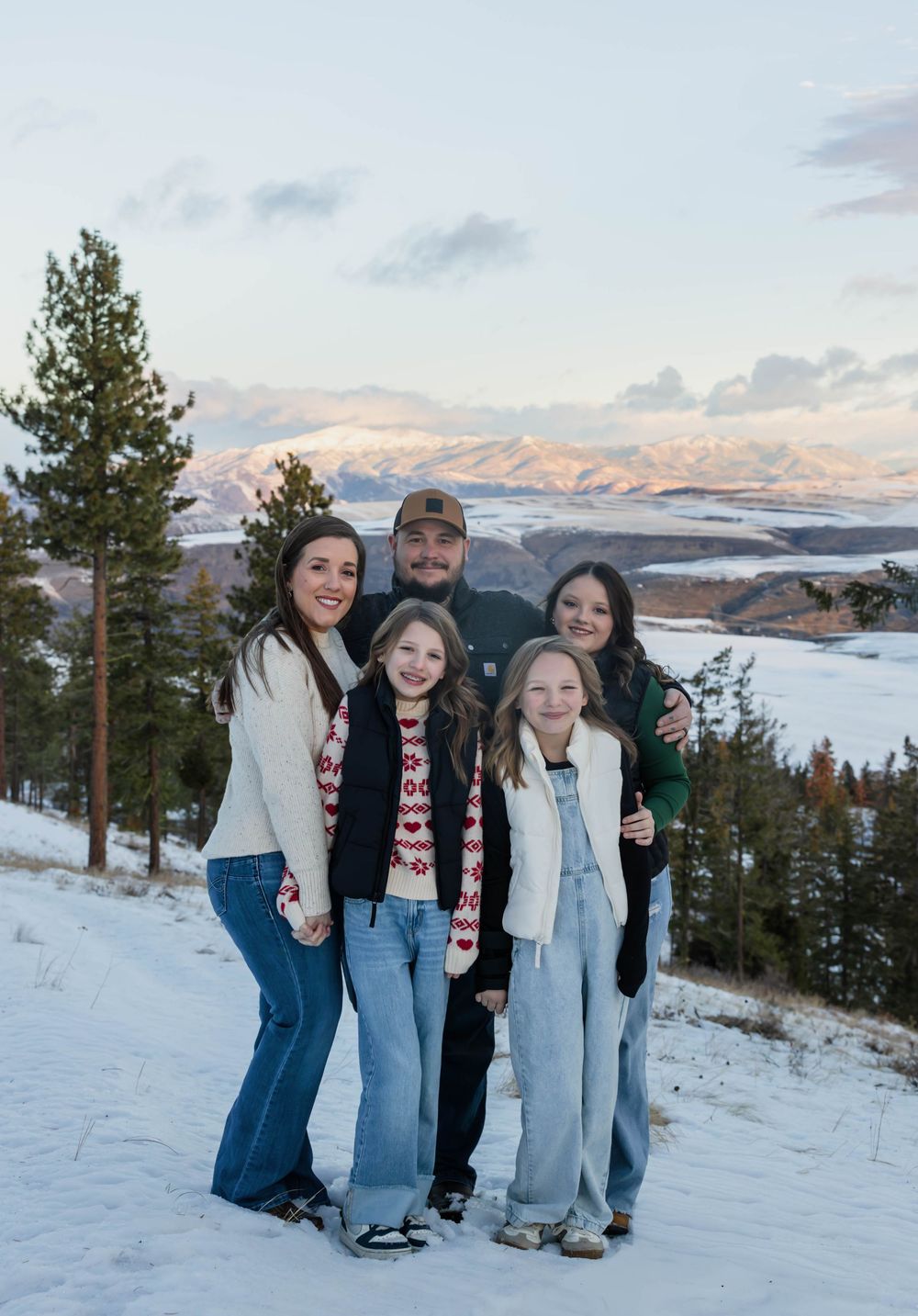 A group poses together on a snowy hillside with mountains and a lake in the background.