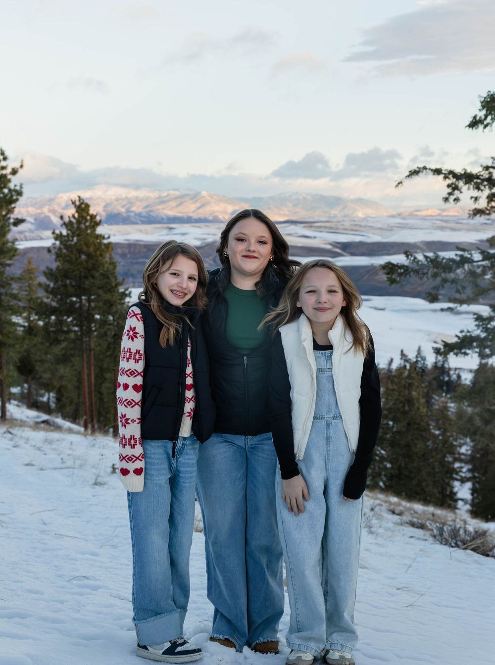 Four people stand together on a snow-covered slope with mountains visible in the distance.