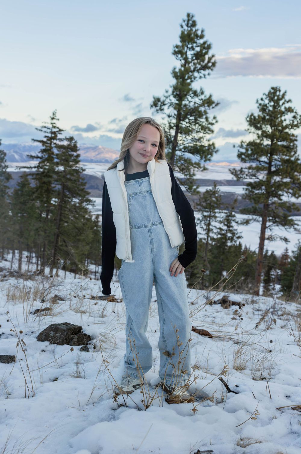 Winter photoshoot on a snow-covered mountain with pine trees and distant lake views.