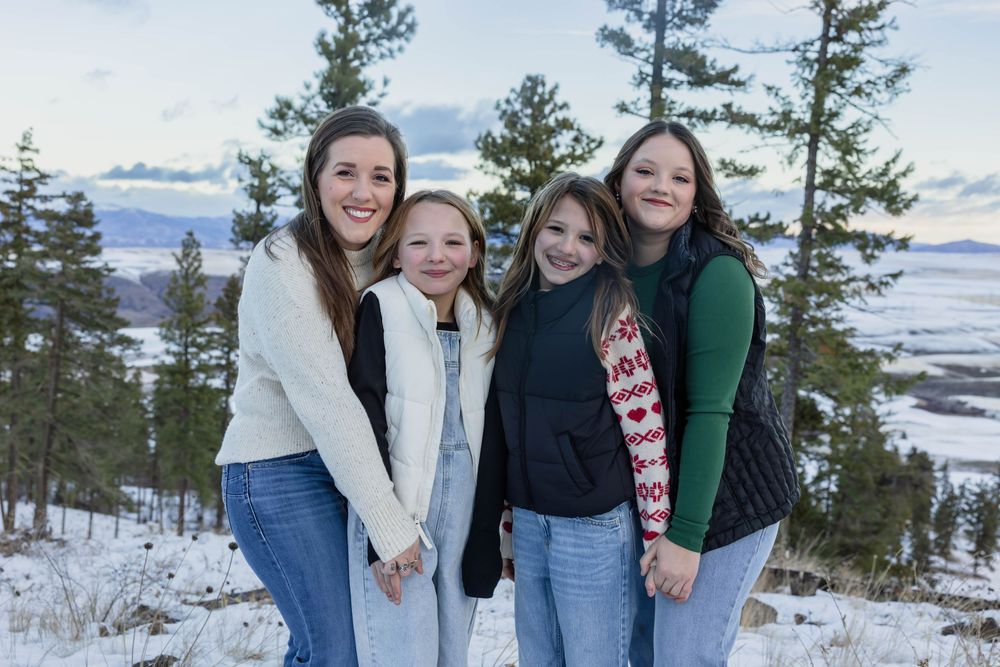 Group photo session in winter with snow-covered mountains and evergreen trees in background.