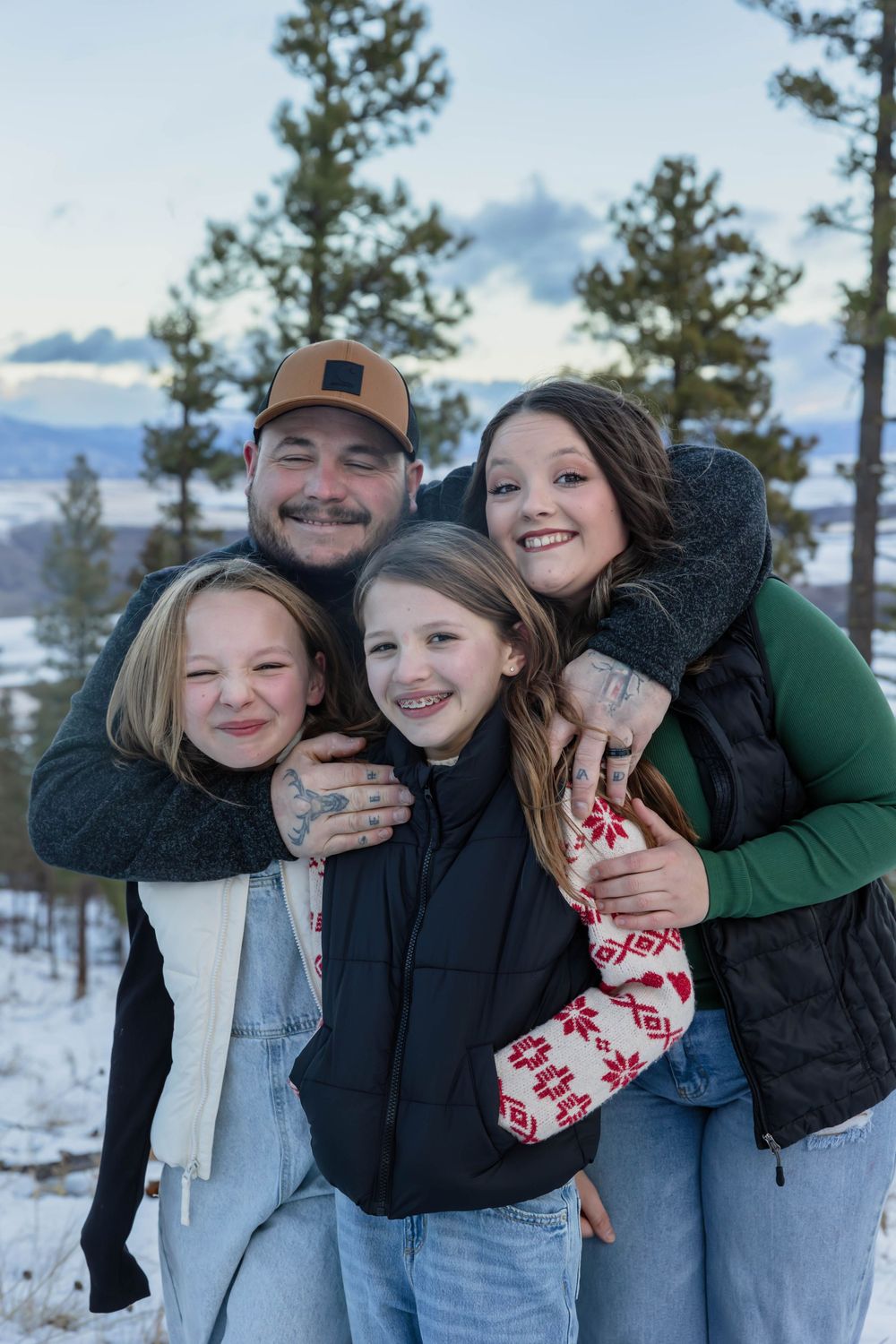 A playful winter photoshoot in the snow with evergreen trees and mountains in the background.