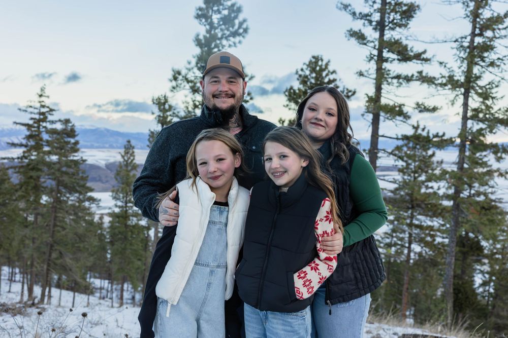 Group poses together against a snowy mountain landscape with pine trees.