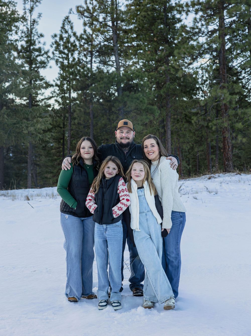 Family photo session in a winter landscape with snow-covered ground and evergreen trees.