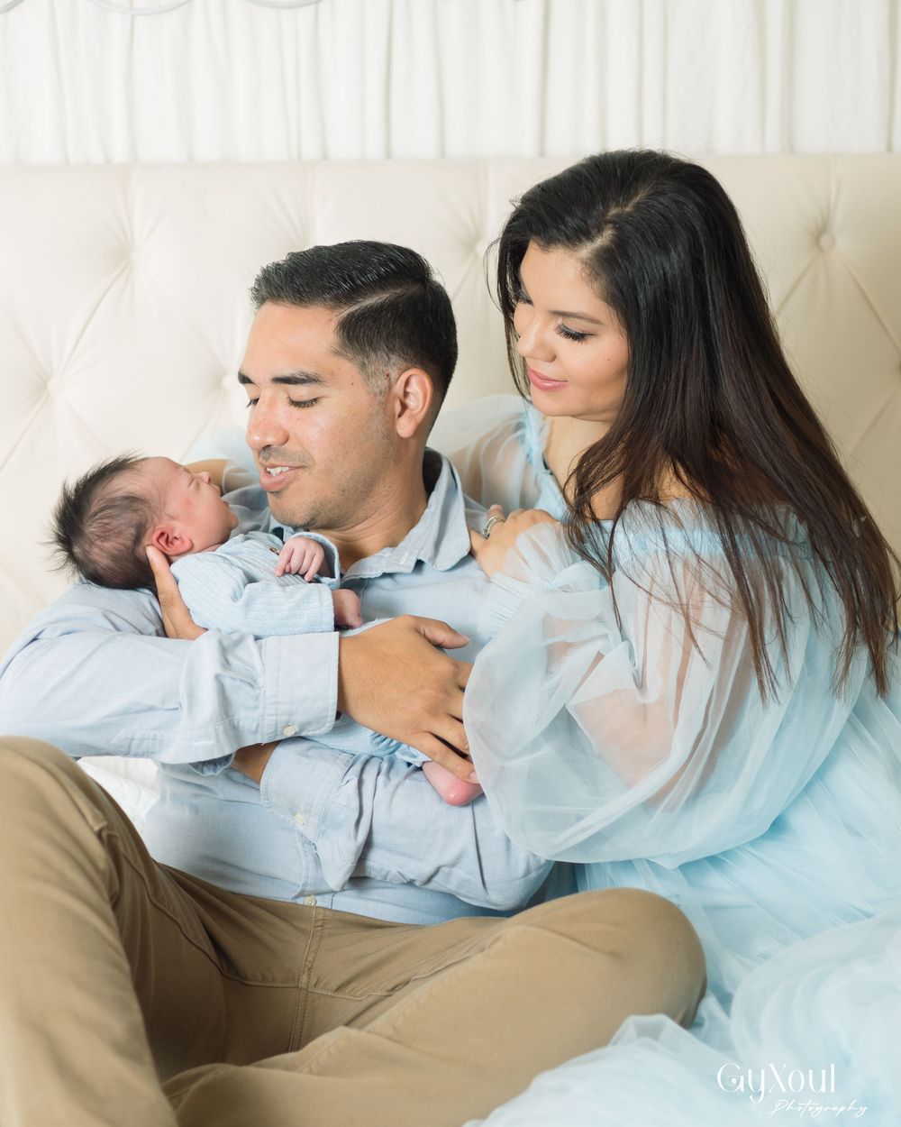A couple rests together on a couch with their newborn baby in a tender family moment.