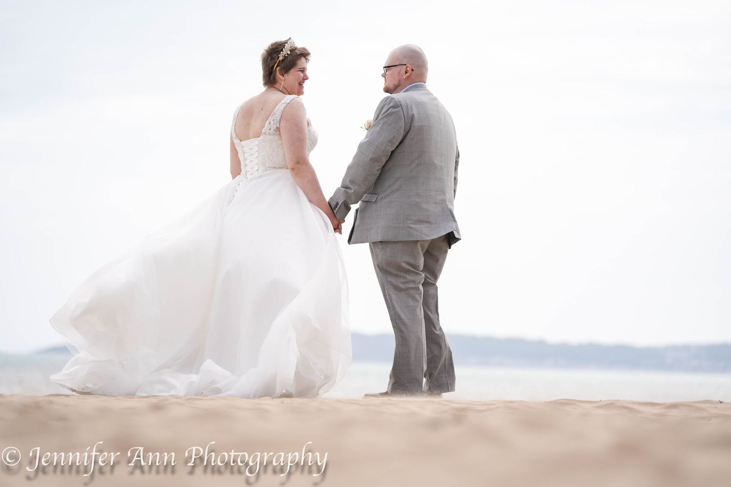 A bride and groom share a romantic moment on a sandy beach at sunset while waves crash in the background.