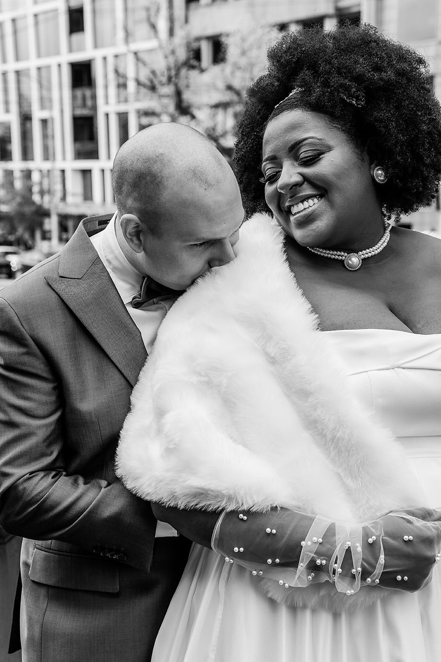 A joyful black and white wedding photo showing a couple embracing, with the bride wearing a white dress and fur wrap.