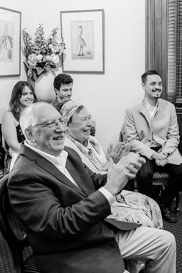 A sequence of black and white photos showing people laughing heartily while sitting together in a room with framed artwork.