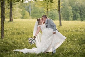 A bride and groom share a romantic moment in a sun-dappled field with trees in the background.