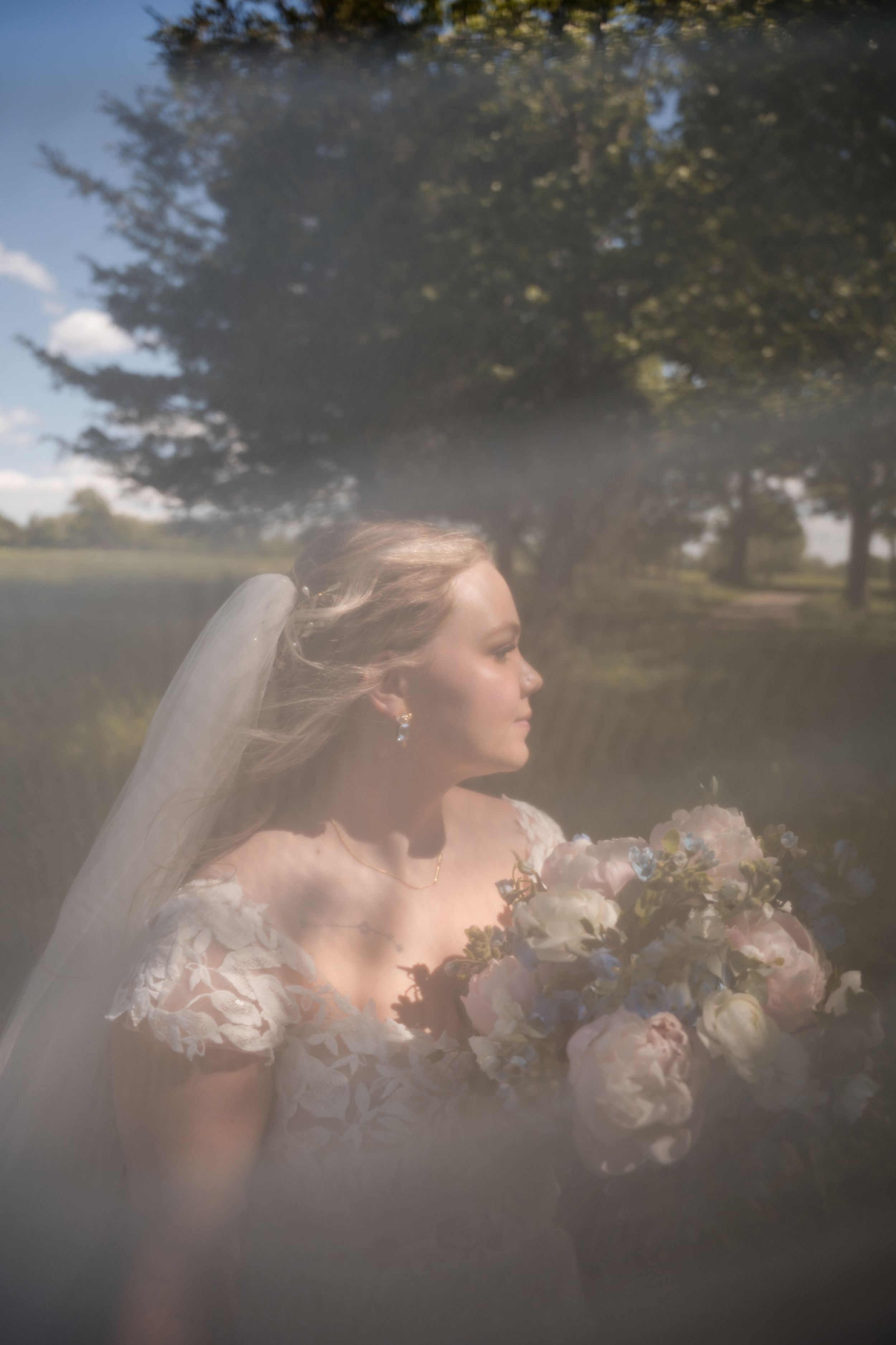 A romantic bridal portrait with a dreamy soft-focus effect showing the bride holding a pastel bouquet in natural sunlight.