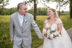 A bride and groom share a happy moment outdoors on their wedding day in a grassy field with trees.