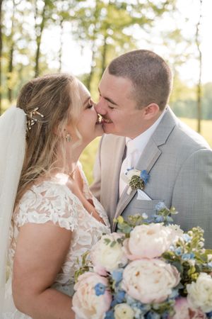 A romantic outdoor wedding photo with cream peonies and blue wildflower bouquet in the foreground.
