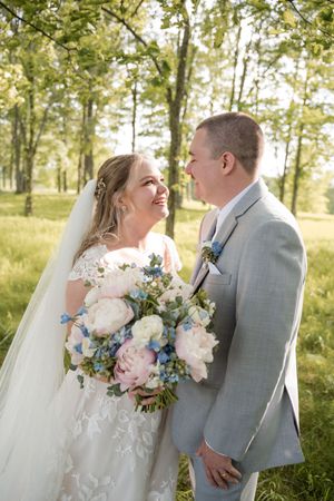 A romantic wedding portrait outdoors showing a bouquet with pink and blue flowers against a natural backdrop.