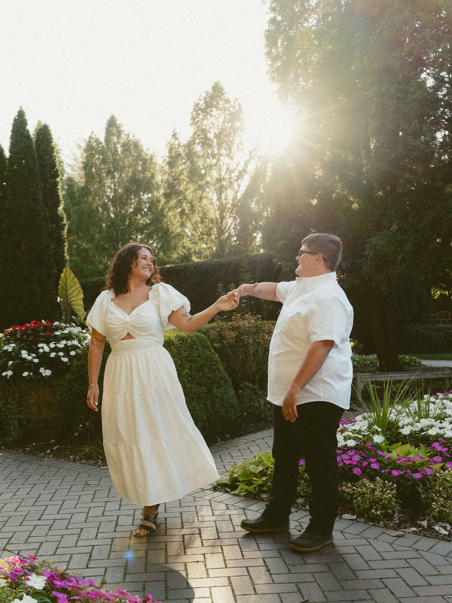 An engagement photo session dancing joyfully together on a stone path surrounded by flowers at sunset at Wegerzyn gardens in Dayton Ohio