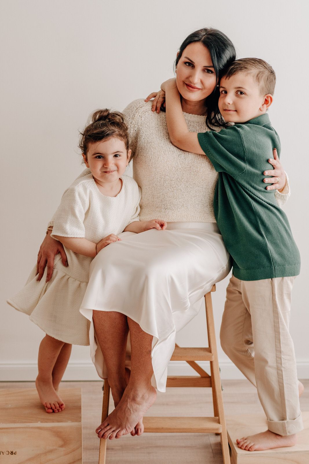 A family portrait in neutral tones showing a tender moment together against a white wall. Familienfotografie Hessen
