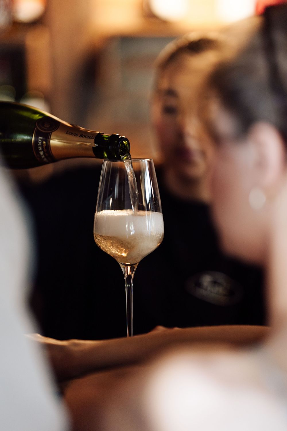 Bartender pouring champagne into an elegant flute glass at a bar.
