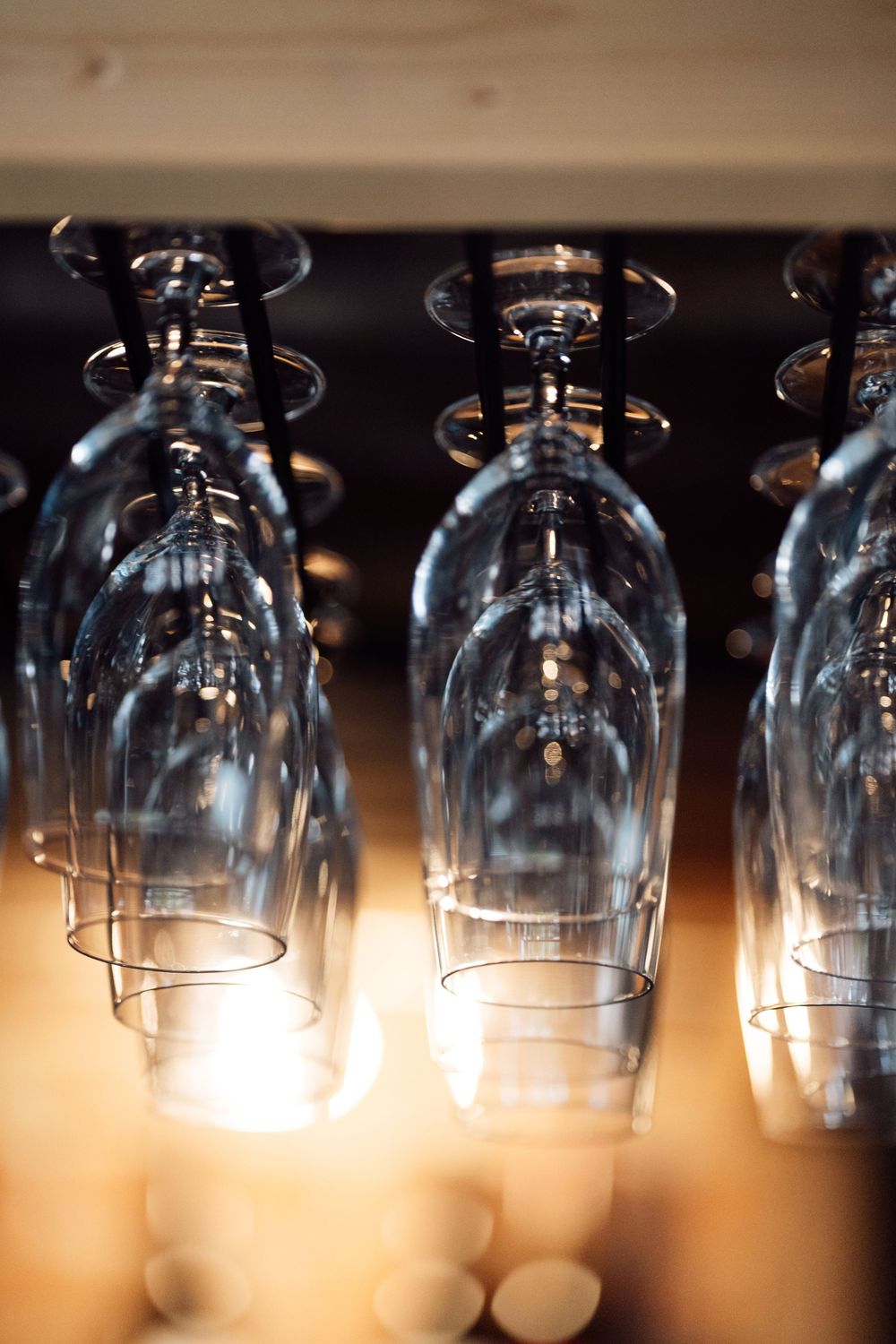 Clean wine glasses stored upside down on a bar rack, illuminated by warm light from below.