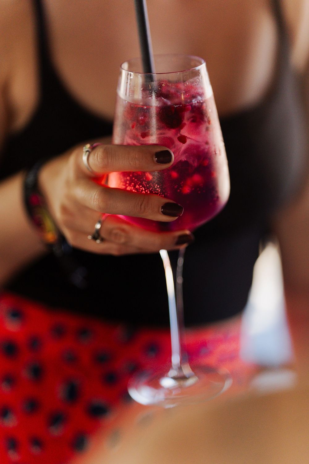 Woman holding a wine glass filled with red berry cocktail, wearing black top and red polka dot skirt.