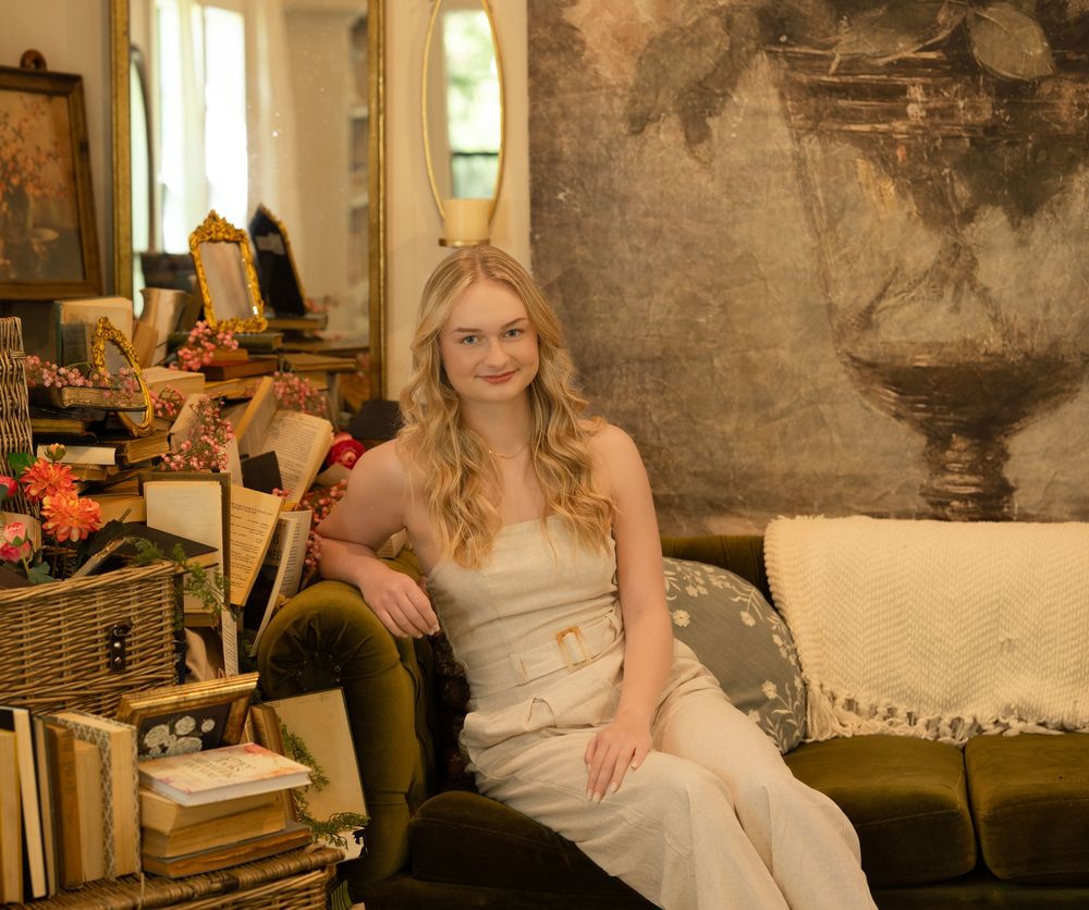A person in a white top relaxes on a vintage couch in a cozy living room filled with antique decor and books.