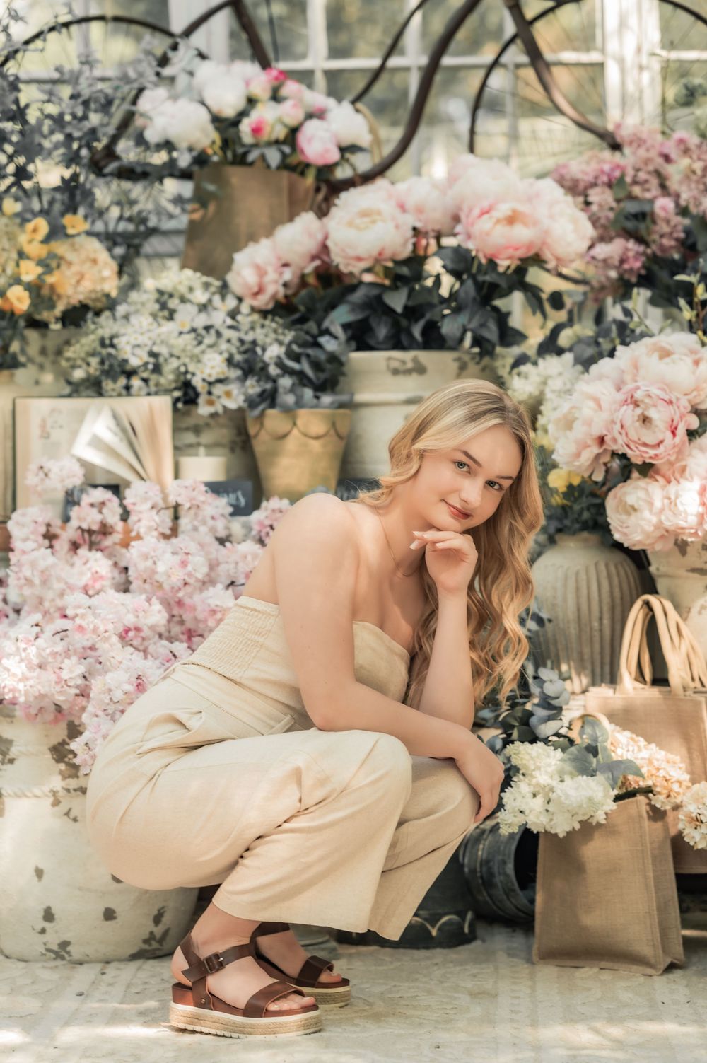 Elegant spring fashion photo with blush pink roses and soft floral arrangements around a beige outfit and shopping bag.