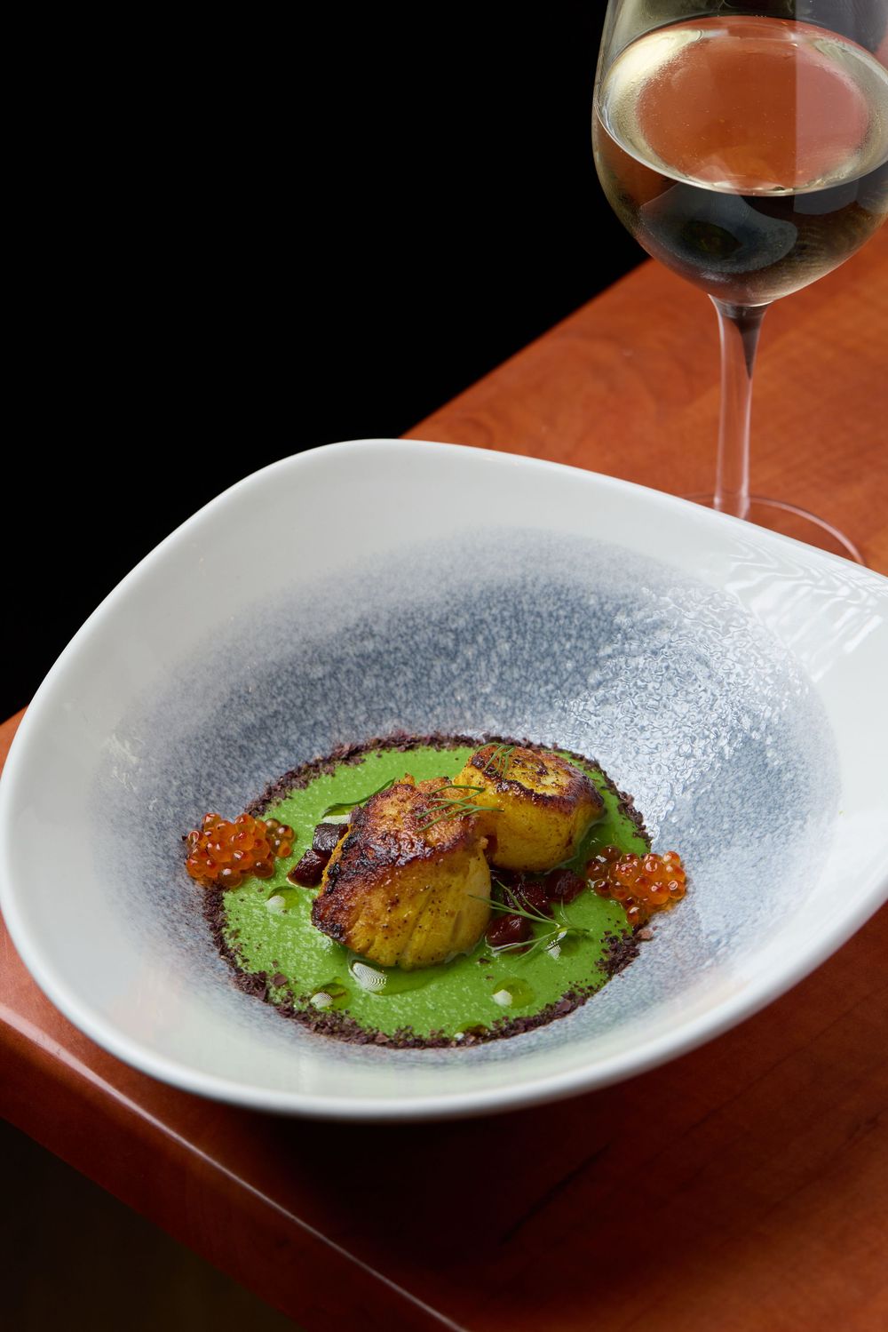 Seared scallops on green puree served in curved white dish with red wine.