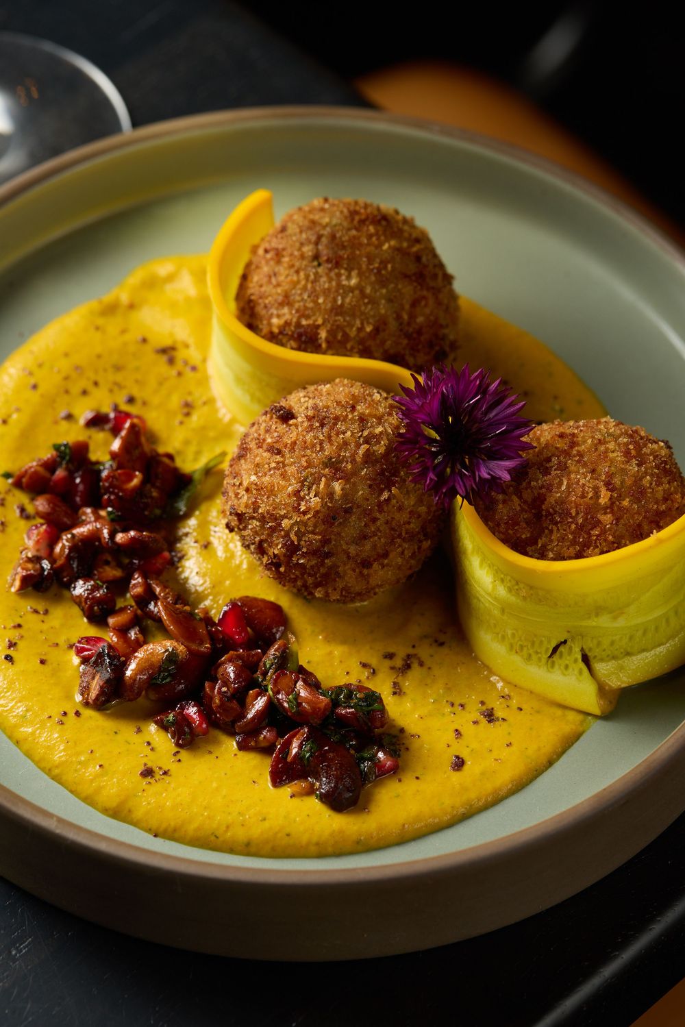 Breaded croquettes on yellow sauce garnished with purple flowers and dark garnish.