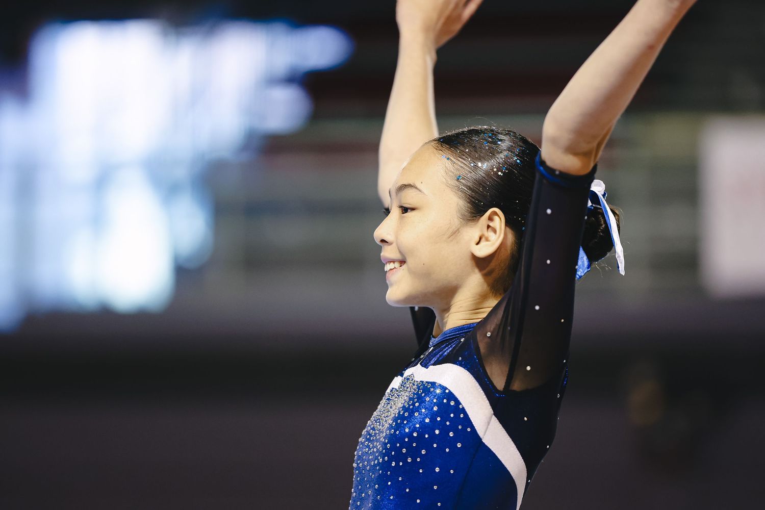 Gymnast in sparkly blue leotard strikes elegant pose during competitive performance at indoor arena.