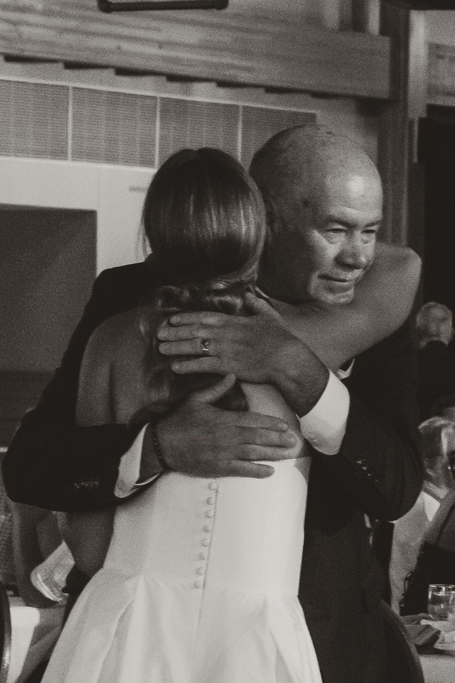 A tender moment captured in black and white as two people share an embrace at what appears to be a wedding reception.