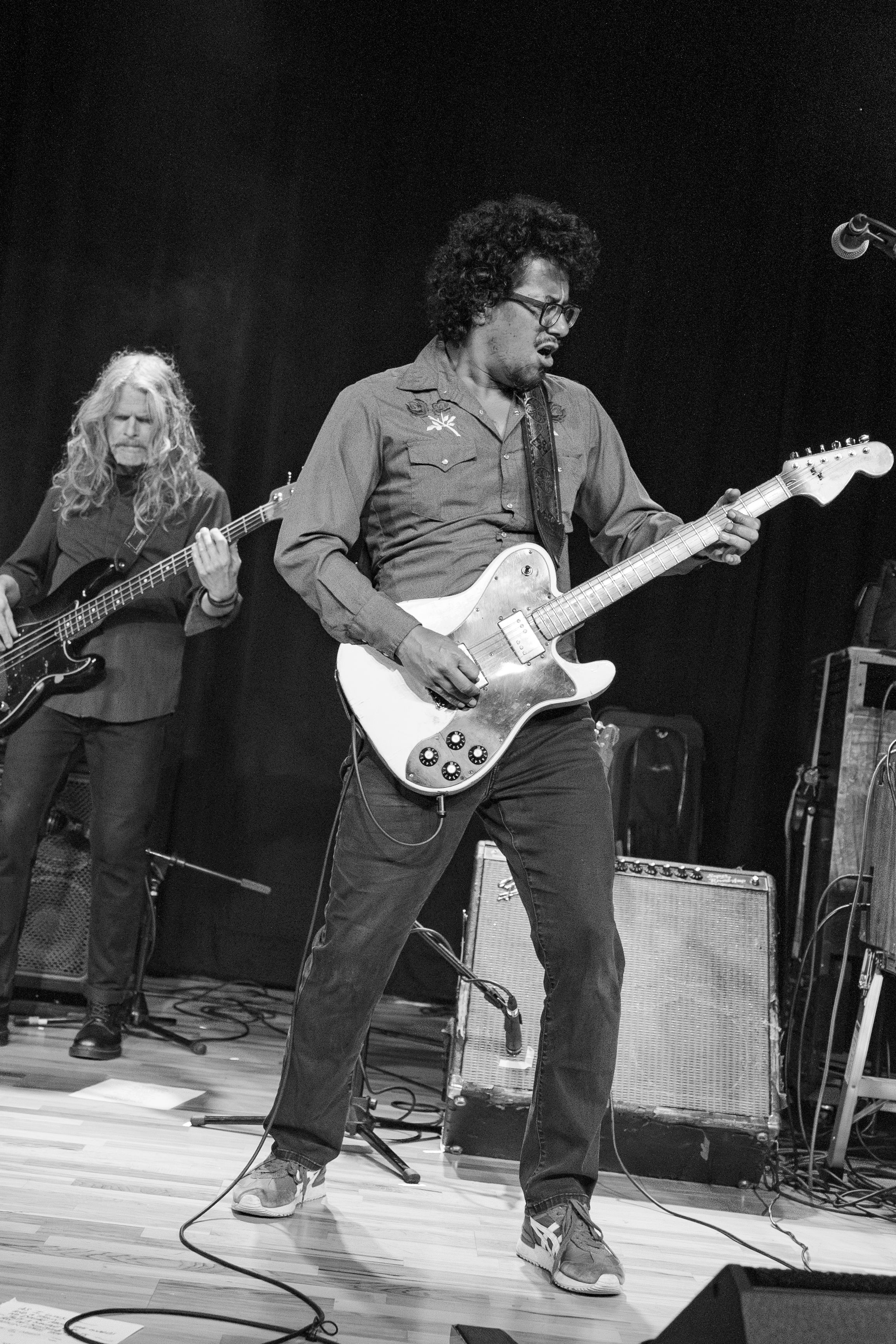 Black and white photo of musicians performing on stage with guitars during a live rock concert performance.