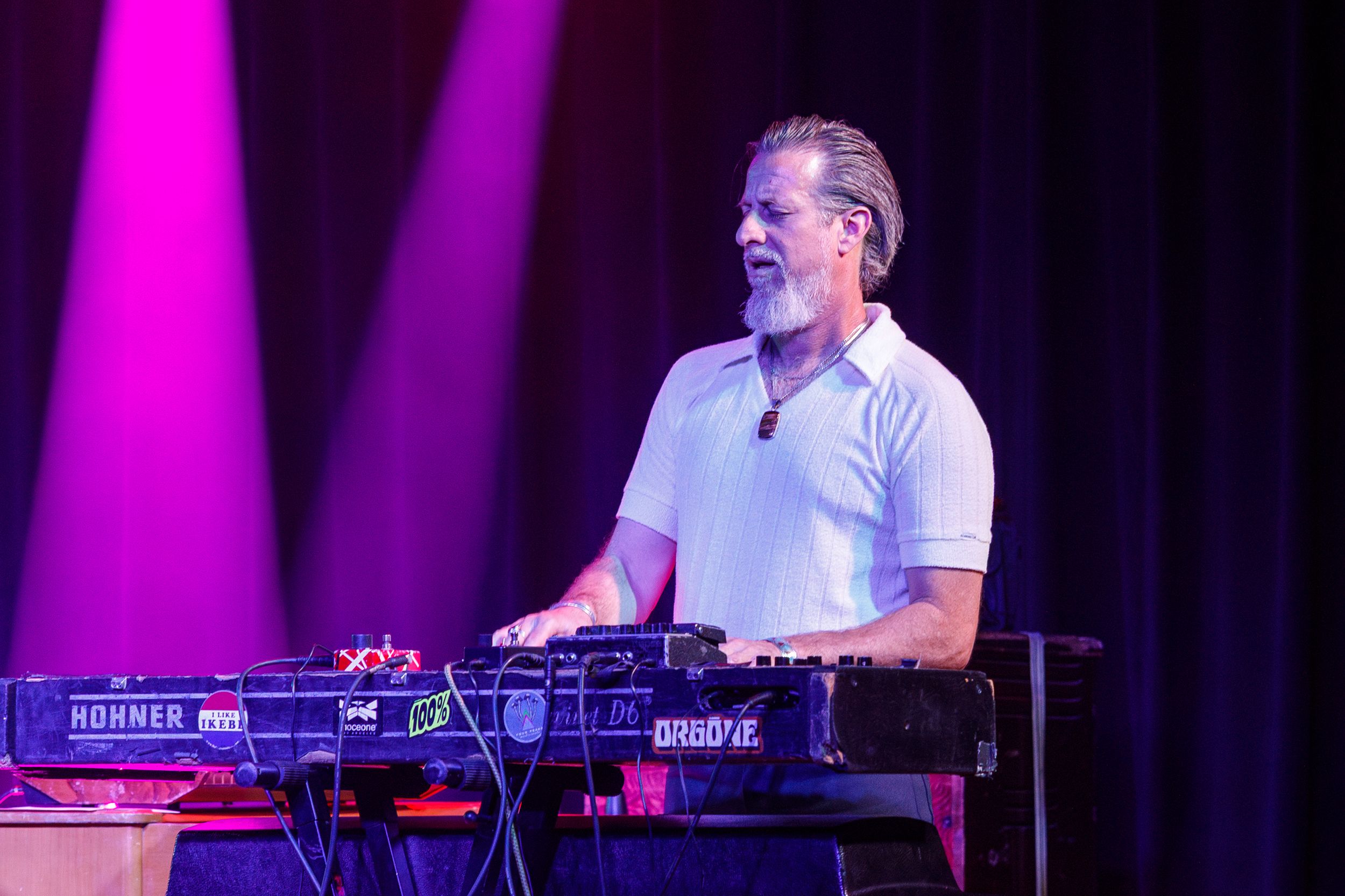 Musician performing on stage with keyboards under bright purple lighting during a concert performance.