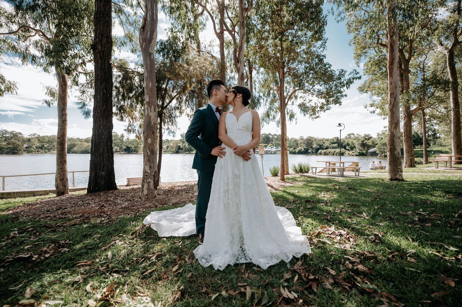 A couple shares an intimate moment on their wedding day by a serene lake, surrounded by tall eucalyptus trees.
