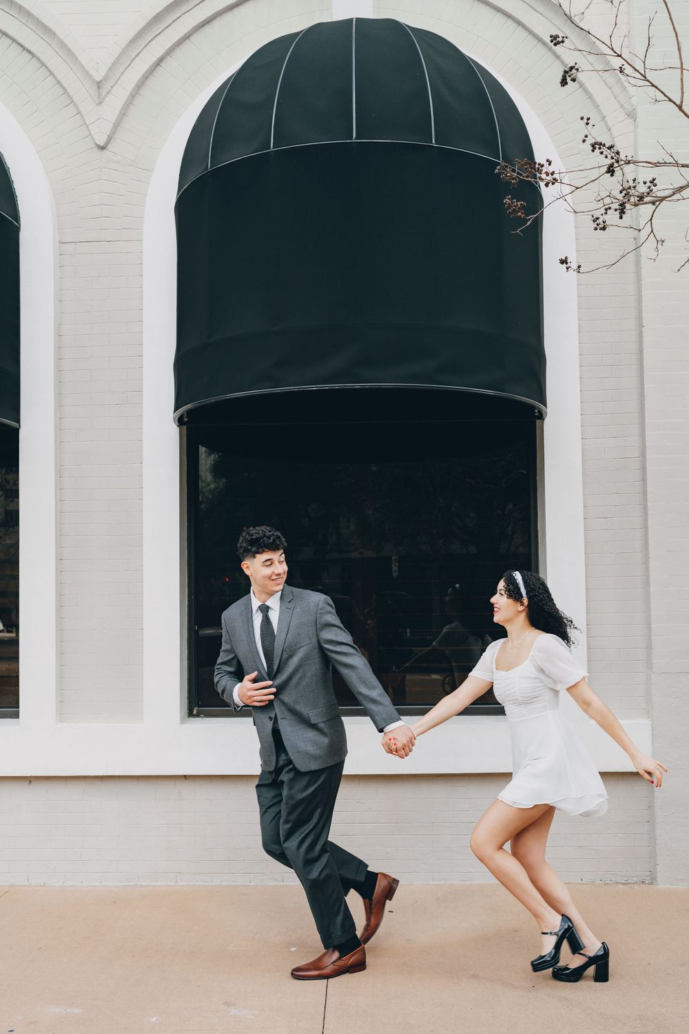 A playful couple dances together beneath a black awning on a sunny day.
