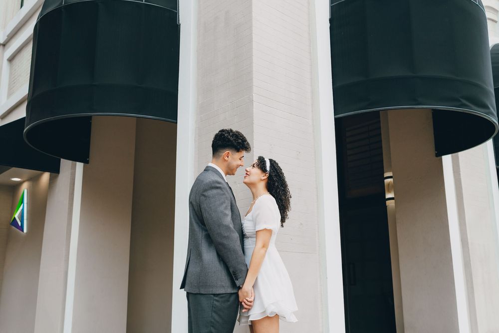 A couple shares a romantic kiss under black awnings outside of an elegant building facade.