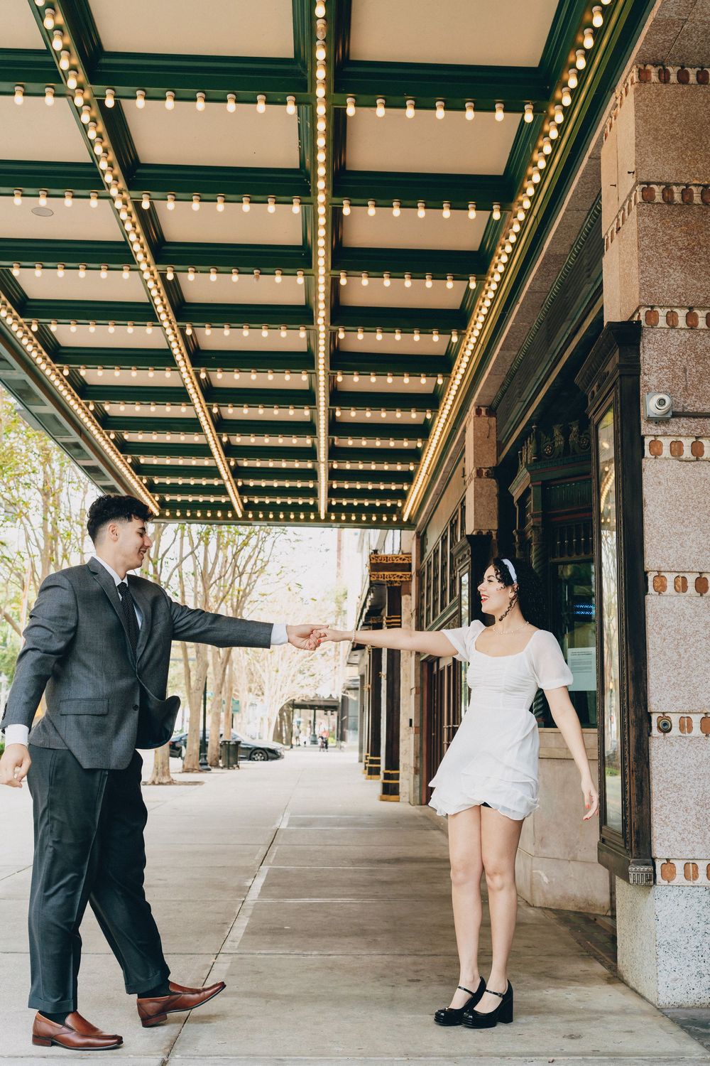 A couple stands under an ornate ceiling with string lights in an elegant outdoor walkway.
